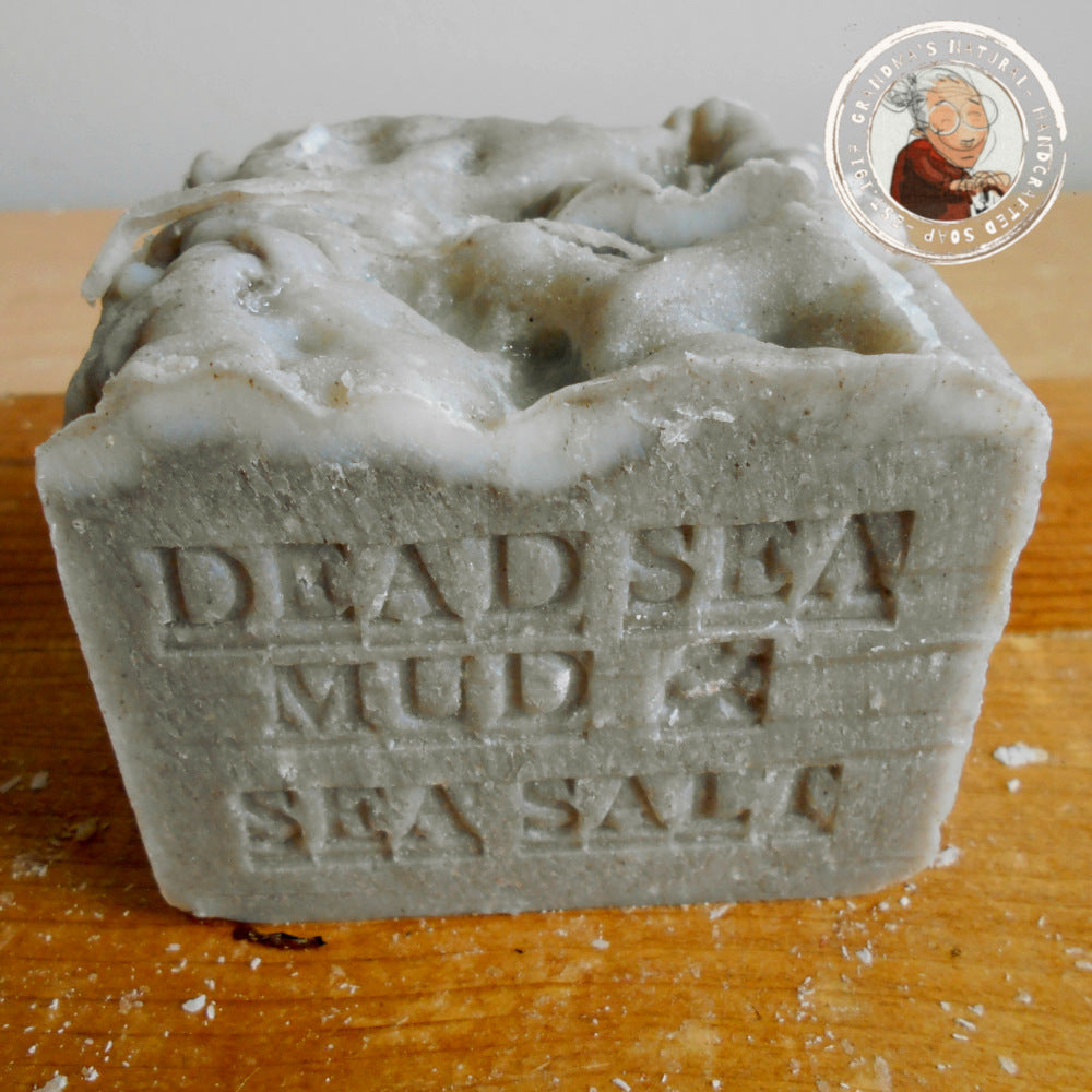 Dead Sea Mud and Sea Salt engraved on it here's a small logo featuring an illustration of a Grandmother. The soap has a textured surface with some speckles of sea salt